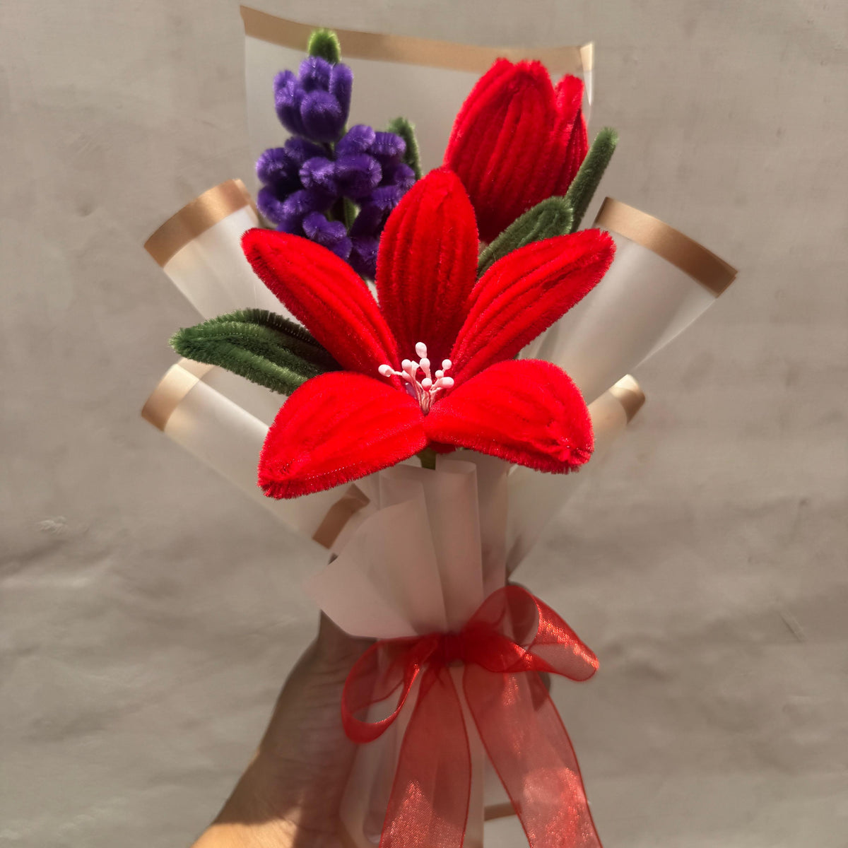 Bouquet with red flowers and a red ribbon held against a gray background